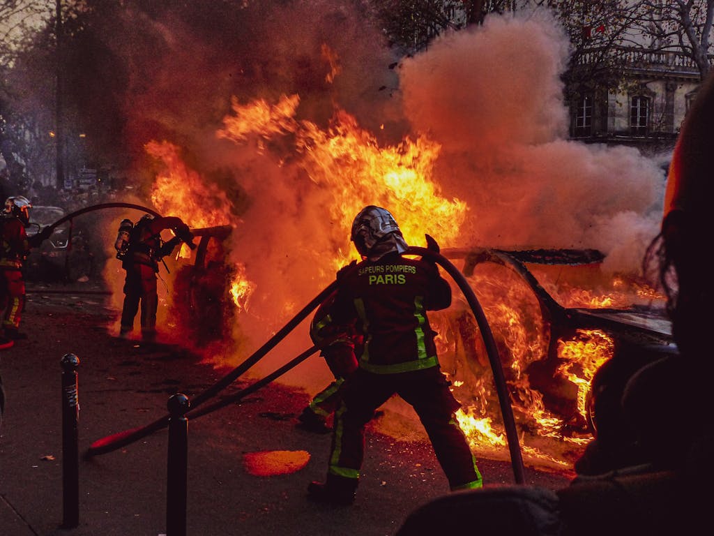 Firefighters extinguishing a blazing car fire on Paris streets during an emergency response.